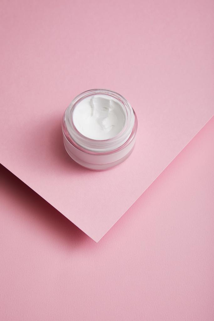 Hochwinkel-Ansicht der kosmetischen Creme im Glas auf rosa Papier strukturierten Hintergrund  - Foto, Bild
