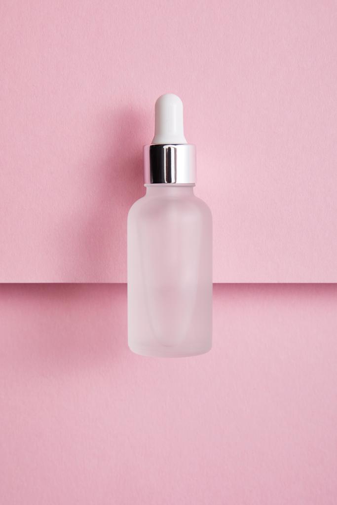 Верхний вид бутылки сыворотки с жидкостью на фоне розовой бумаги
 - Фото, изображение