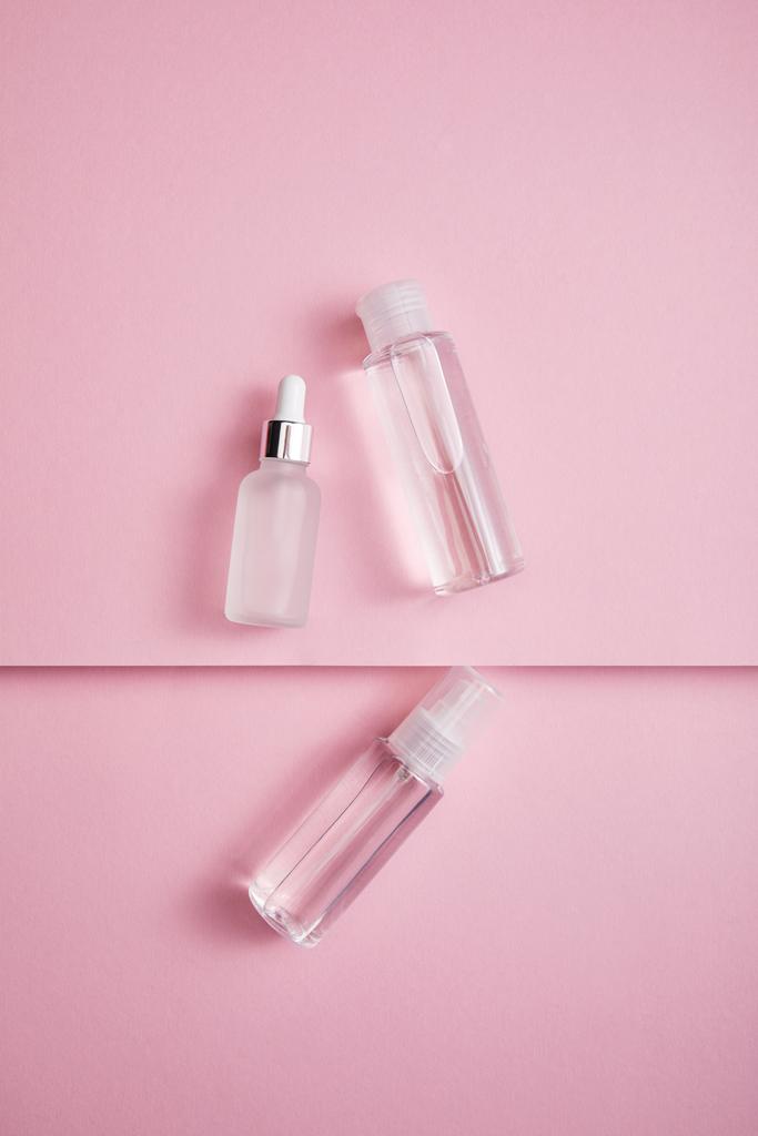 Вид сверху прозрачной косметической бутылки, спрея и флакона сыворотки с жидкостью на розовом бумажном фоне
 - Фото, изображение