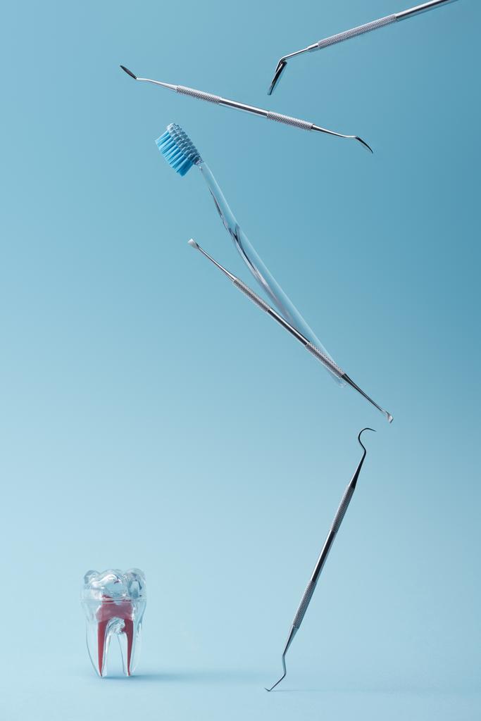Metal dental instruments, toothbrush and artificial tooth model on blue background - Photo, Image
