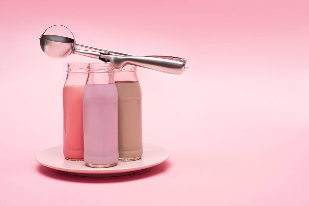 Bottles of berry, strawberry and chocolate milkshakes with scoop on plate on pink background - Photo, Image