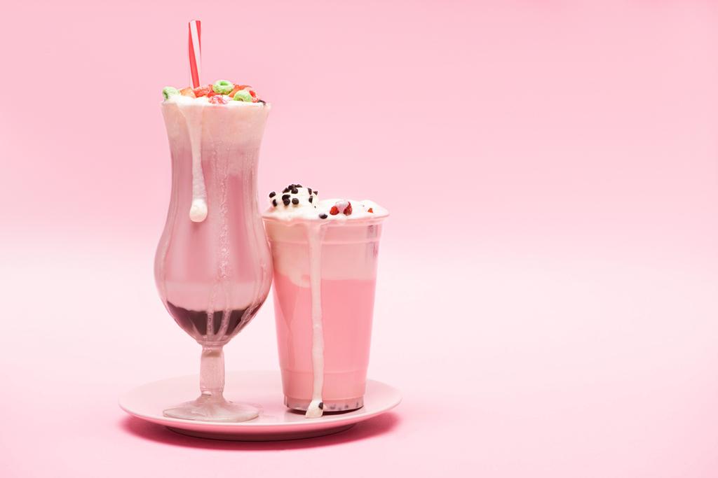 ピンクの背景にプレート上のイチゴミルクセーキの使い捨てカップとガラス - 写真・画像