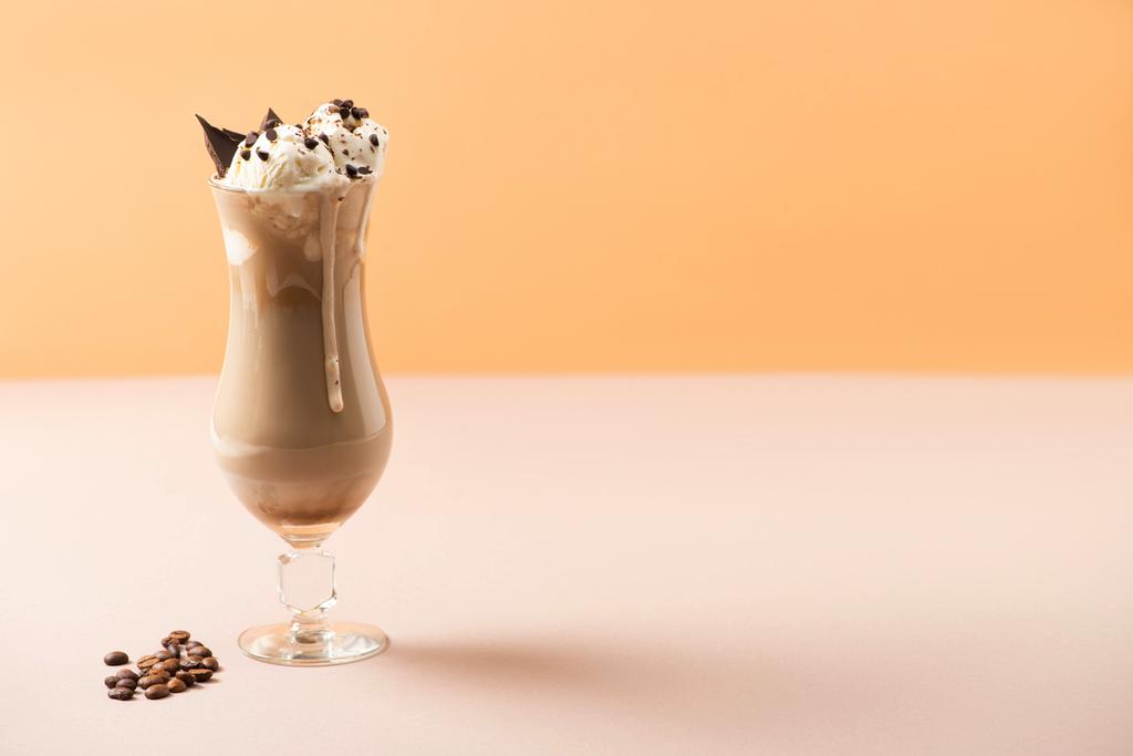 Verre de milkshake avec crème glacée et morceaux de chocolat près des grains de café sur beige et orange
 - Photo, image