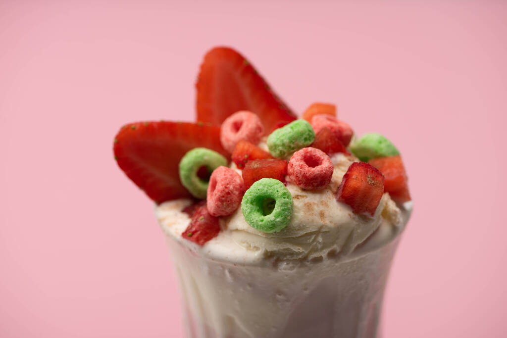 Selective focus of glass of milkshake with ice cream, cut strawberries and candies isolated on pink - Photo, Image