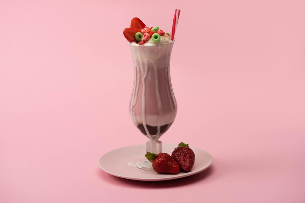 Copo de milkshake com palha de bebida, doces e morangos no prato no fundo rosa
 - Foto, Imagem
