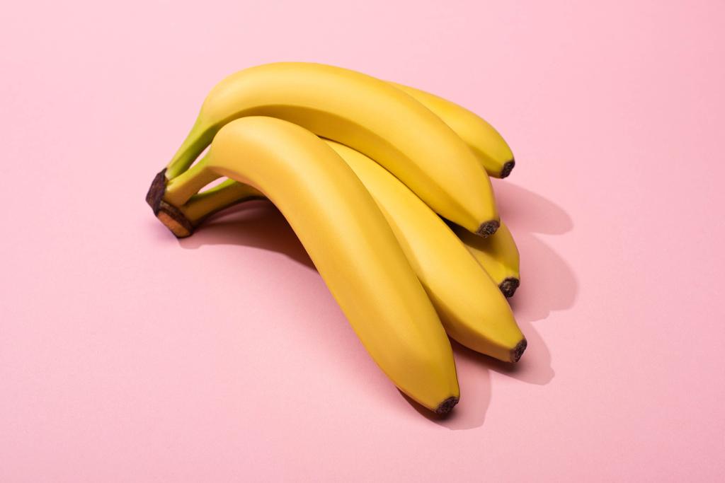 Vista de ángulo alto de plátanos amarillos maduros sobre fondo rosa
 - Foto, imagen