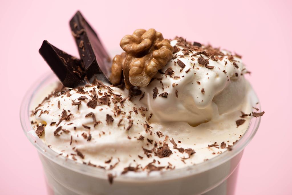 Одноразова чашка молочного коктейлю з морозивом, горіхом, шоколадною стружкою та шматочками на рожевому фоні
 - Фото, зображення