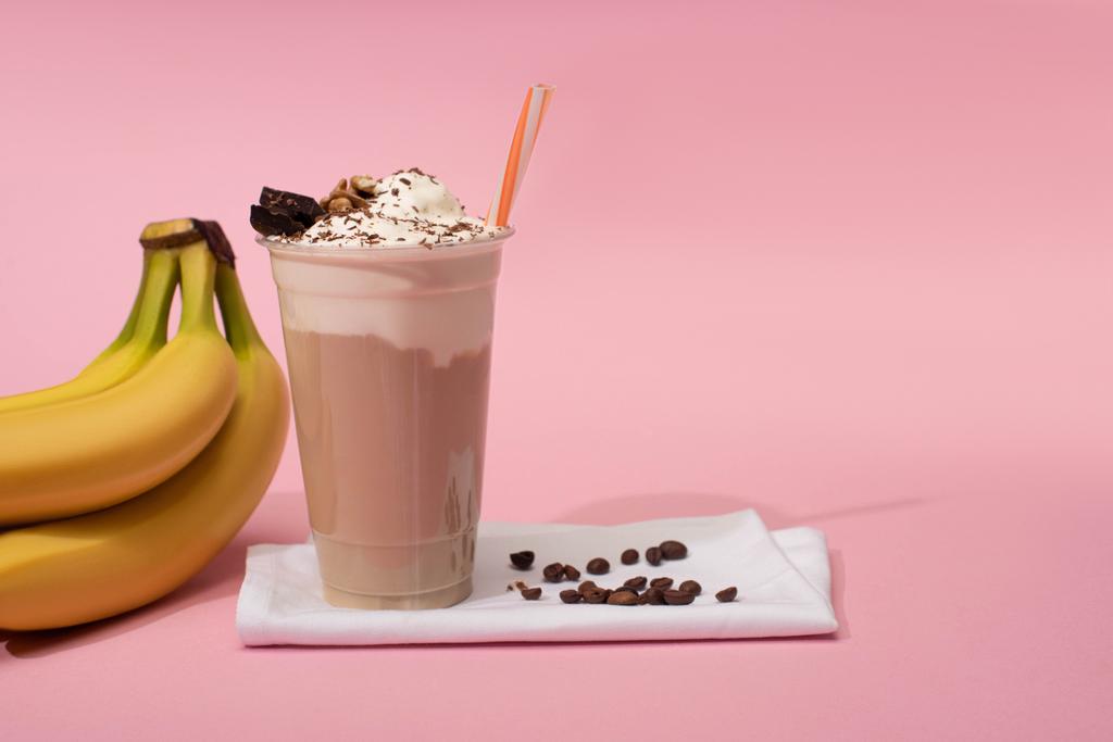 Tazza usa e getta di frullato al cioccolato con chicchi di caffè sui tovaglioli vicino alle banane su rosa
 - Foto, immagini