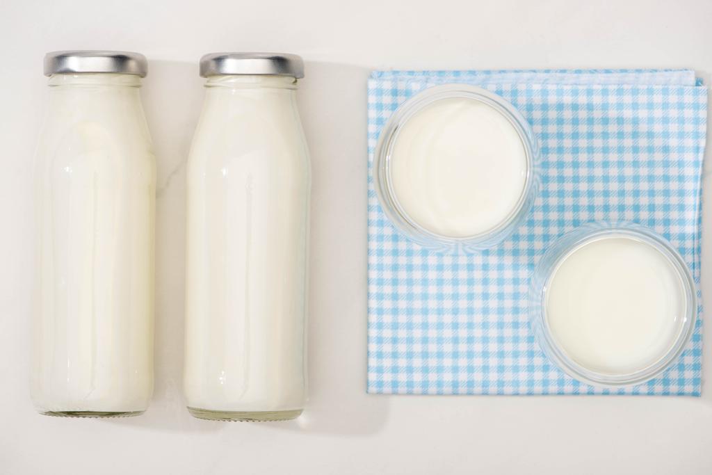 Vista superior de botellas y vasos de yogur casero sobre tela a cuadros sobre fondo blanco
 - Foto, Imagen