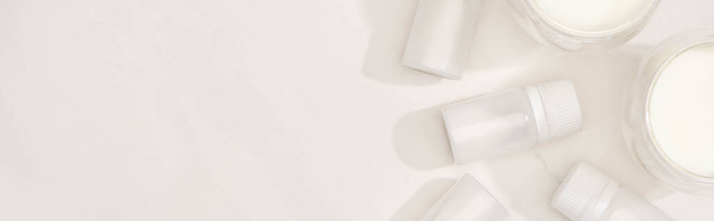 Vista superior de vasos de yogur casero cerca de contenedores con cultivos de iniciación sobre fondo blanco, plano panorámico
 - Foto, Imagen