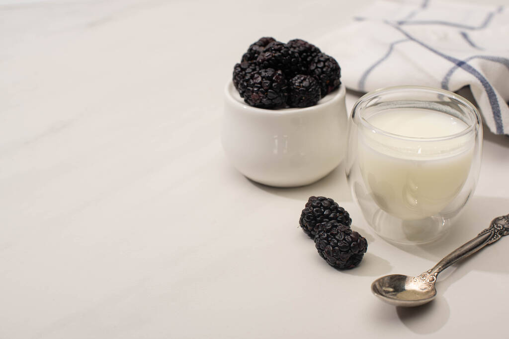 Focus selettivo di zuccheriera con more vicino a un bicchiere di yogurt fatto in casa e cucchiaino su sfondo bianco
 - Foto, immagini