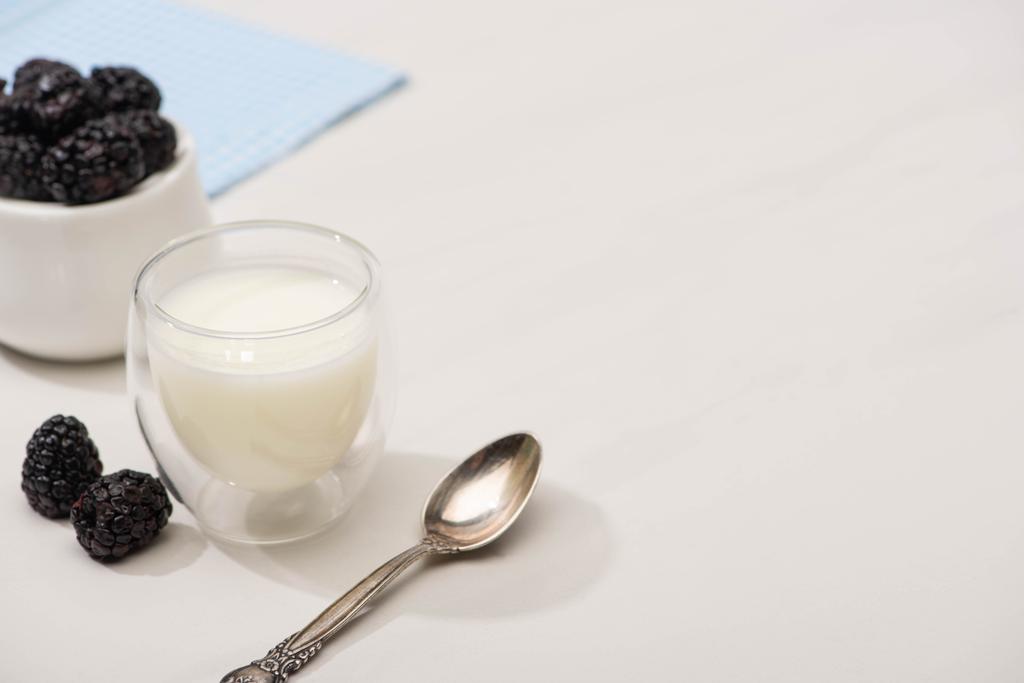 Vista ad alto angolo di cucchiaino, bicchiere di yogurt fatto in casa e zuccheriera con more su bianco
  - Foto, immagini