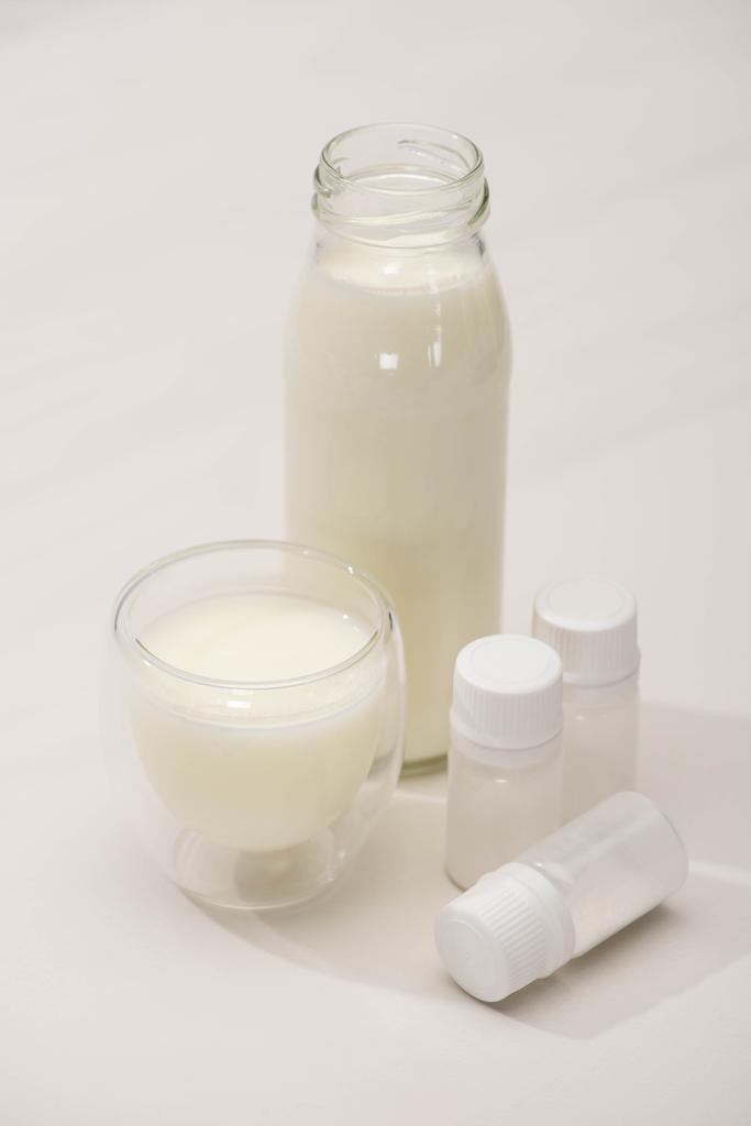 Hoge hoek uitzicht op fles en glas zelfgemaakte yoghurt in de buurt van containers met voorgerecht culturen op witte achtergrond - Foto, afbeelding