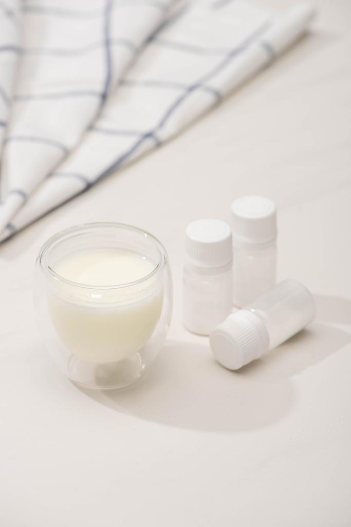Селективный фокус стекла из домашнего йогурта и контейнеров с закуски культур вблизи ткани на белом фоне
 - Фото, изображение