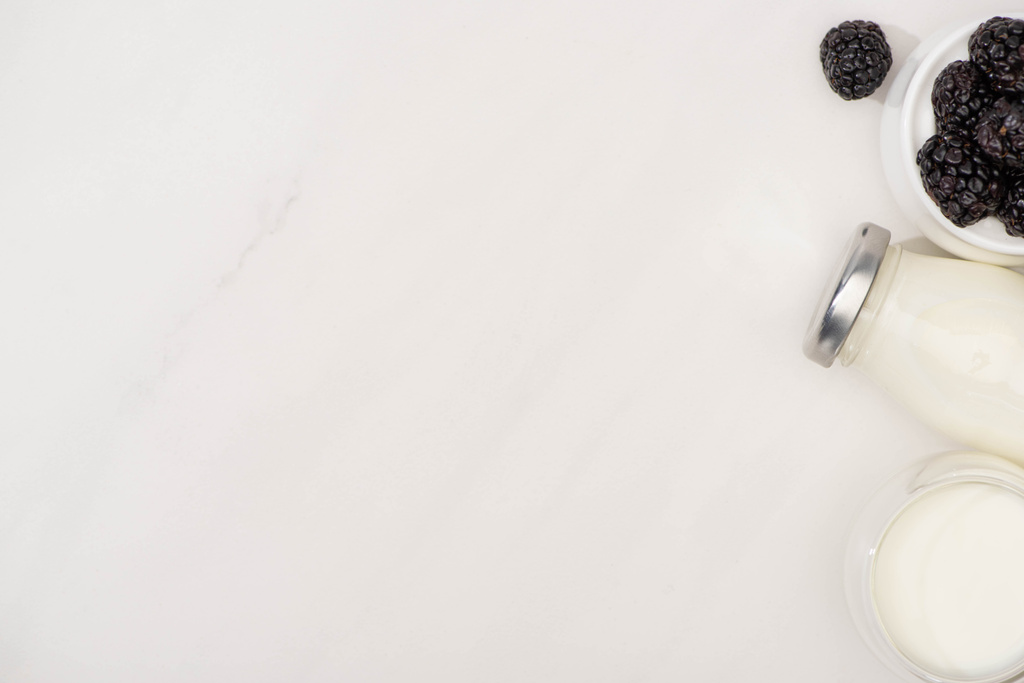 Top view of bottle and glass of homemade yogurt near sugar bowl with blackberries on white background - Photo, Image