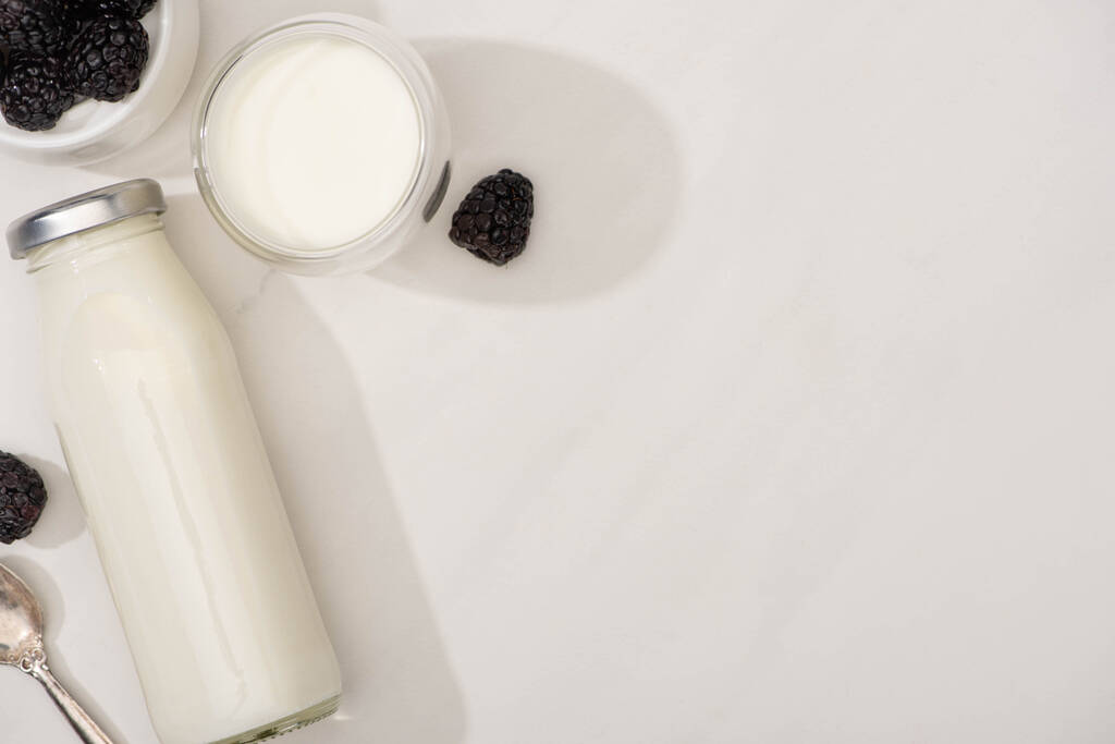 Вид зверху пляшки та келиха домашнього йогурту з ожиною на білому тлі
 - Фото, зображення