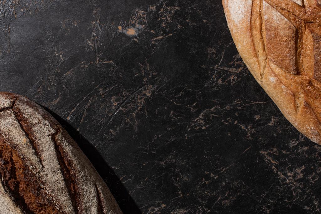 πάνω όψη του φρέσκου ψημένου λευκού και καφέ ψωμιού στην πέτρινη μαύρη επιφάνεια - Φωτογραφία, εικόνα