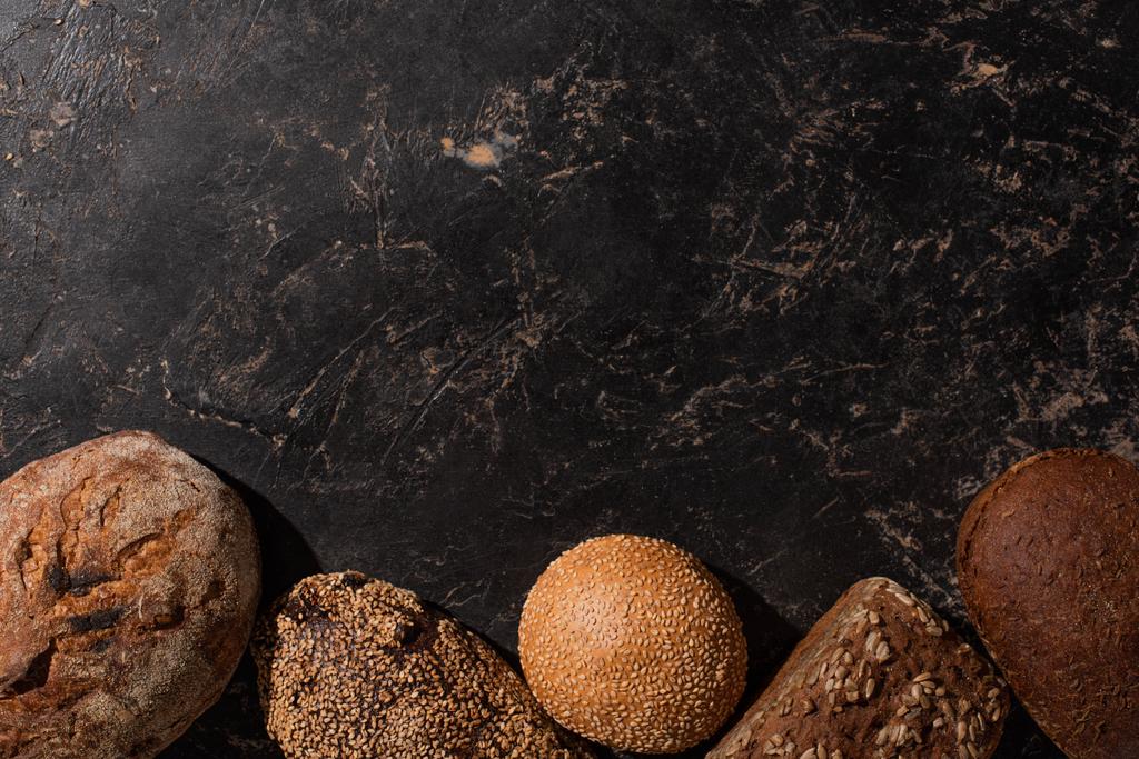 vrchní pohled na čerstvě upečený chléb na kamenném černém povrchu - Fotografie, Obrázek