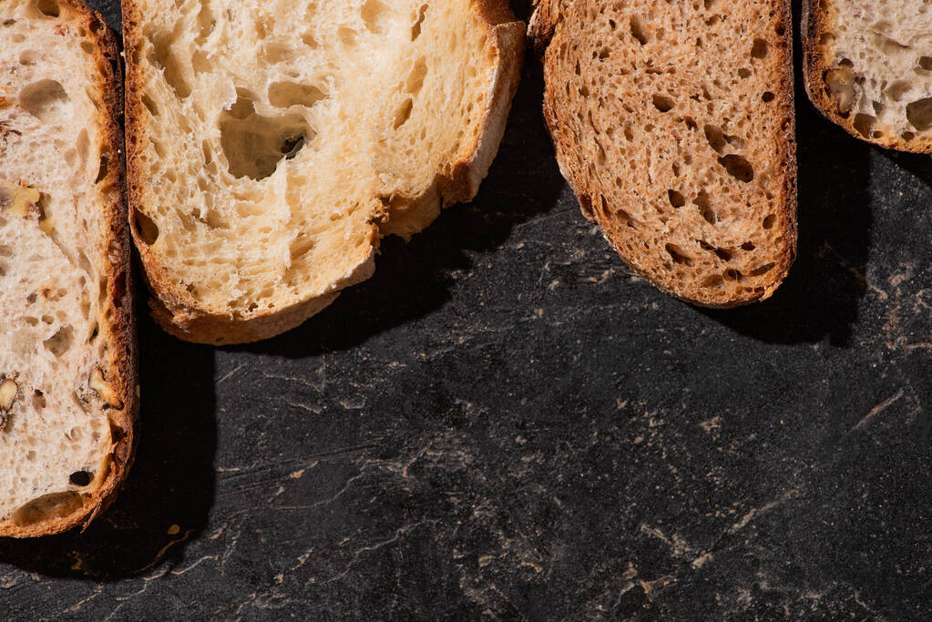 bovenaanzicht van vers gebakken brood plakjes op stenen zwarte ondergrond - Foto, afbeelding