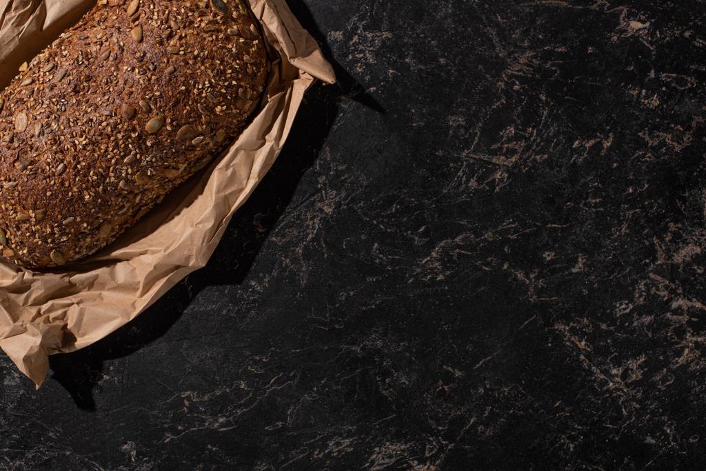 vista superior de la hogaza recién horneada de pan de grano entero en papel sobre la superficie de piedra negro
 - Foto, Imagen