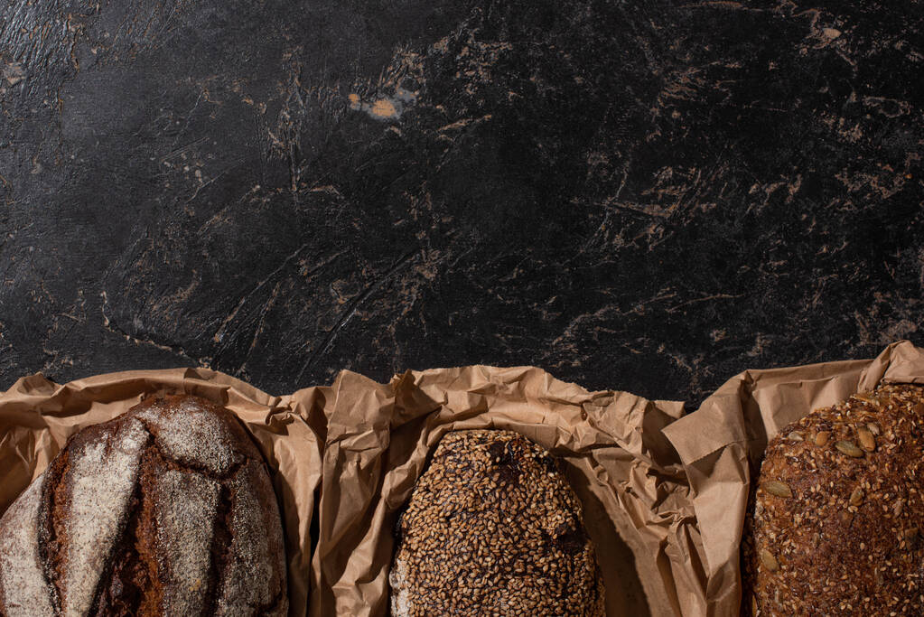 вид зверху свіжого запеченого цілого хліба хлібного хліба в папері на кам'яній чорній поверхні
 - Фото, зображення