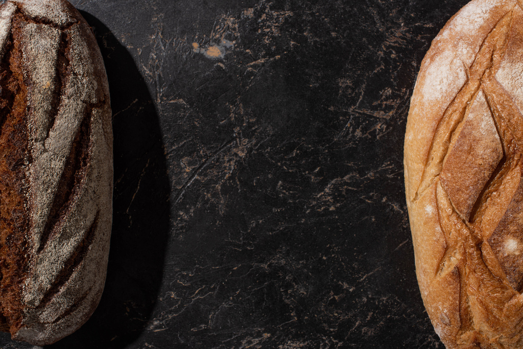 felülnézet friss sült barna és fehér kenyér kő fekete felületen - Fotó, kép
