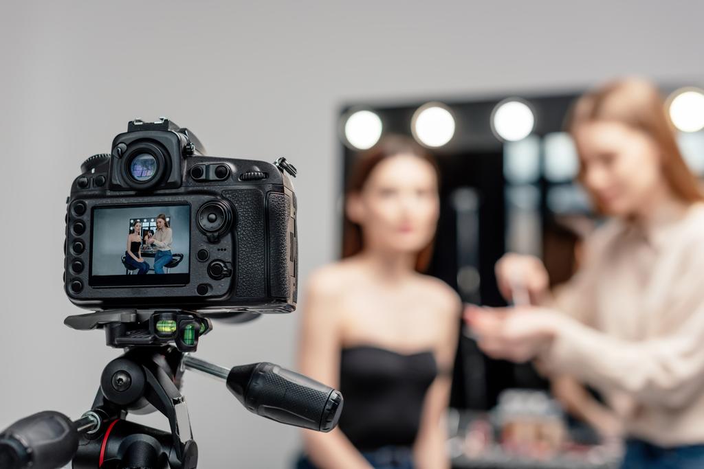 digitaalikameran valikoiva tarkennus, jossa meikkitaiteilija pitää huulikiiltoa lähellä mallia näytöllä eristettynä harmaalla
  - Valokuva, kuva