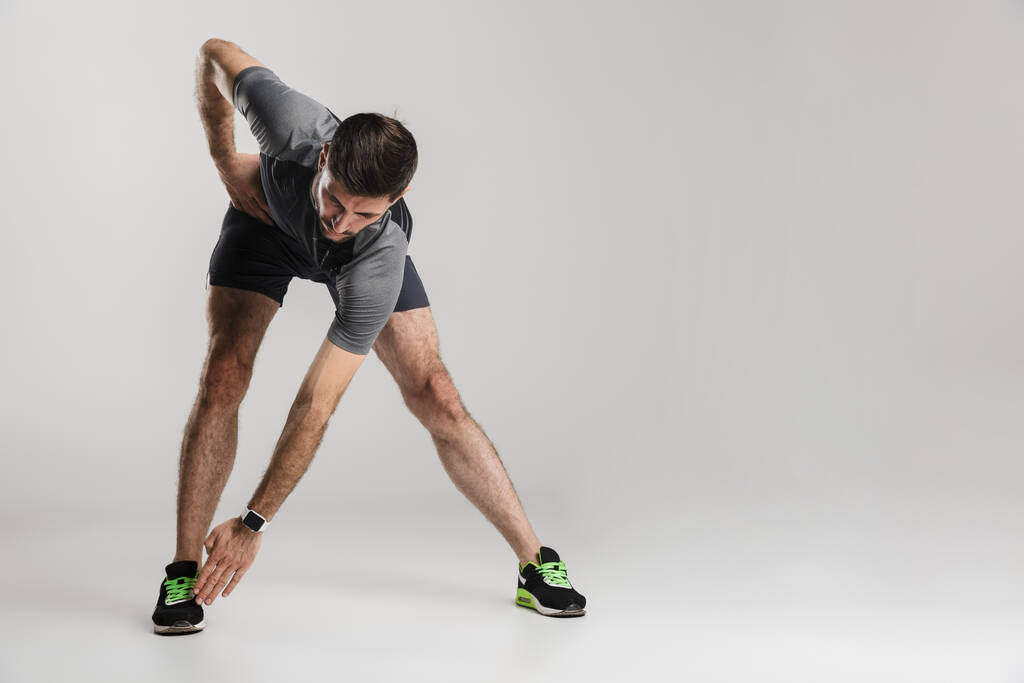 Imagen de hombre atlético caucásico en ropa deportiva haciendo ejercicio mientras hace ejercicio aislado sobre fondo gris
 - Foto, Imagen