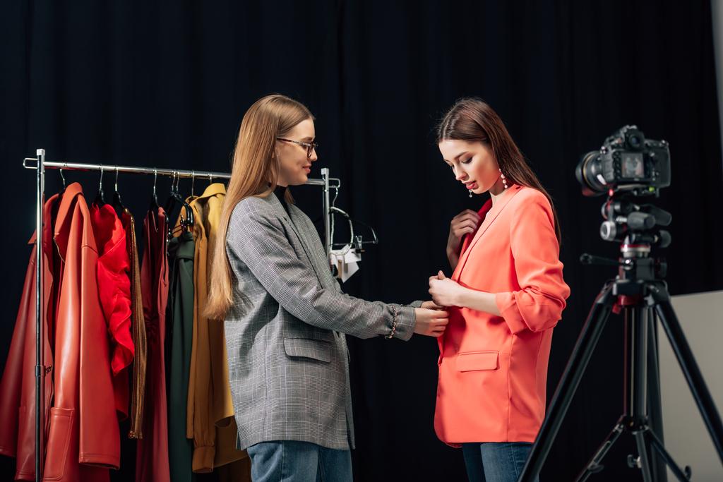 избирательный фокус красивого стилиста в очках касающихся модной куртки на привлекательной модели рядом с цифровой камерой
  - Фото, изображение