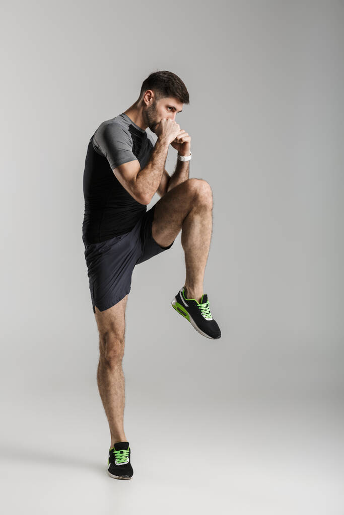 Imagem de homem atlético caucasiano em sportswear fazendo exercício enquanto trabalhava isolado sobre fundo cinza
 - Foto, Imagem