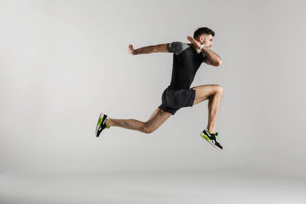 Εικόνα του καυκάσιου αθλητή με αθλητικά να πηδάει ενώ γυμνάζεται απομονωμένος πάνω σε γκρι φόντο - Φωτογραφία, εικόνα