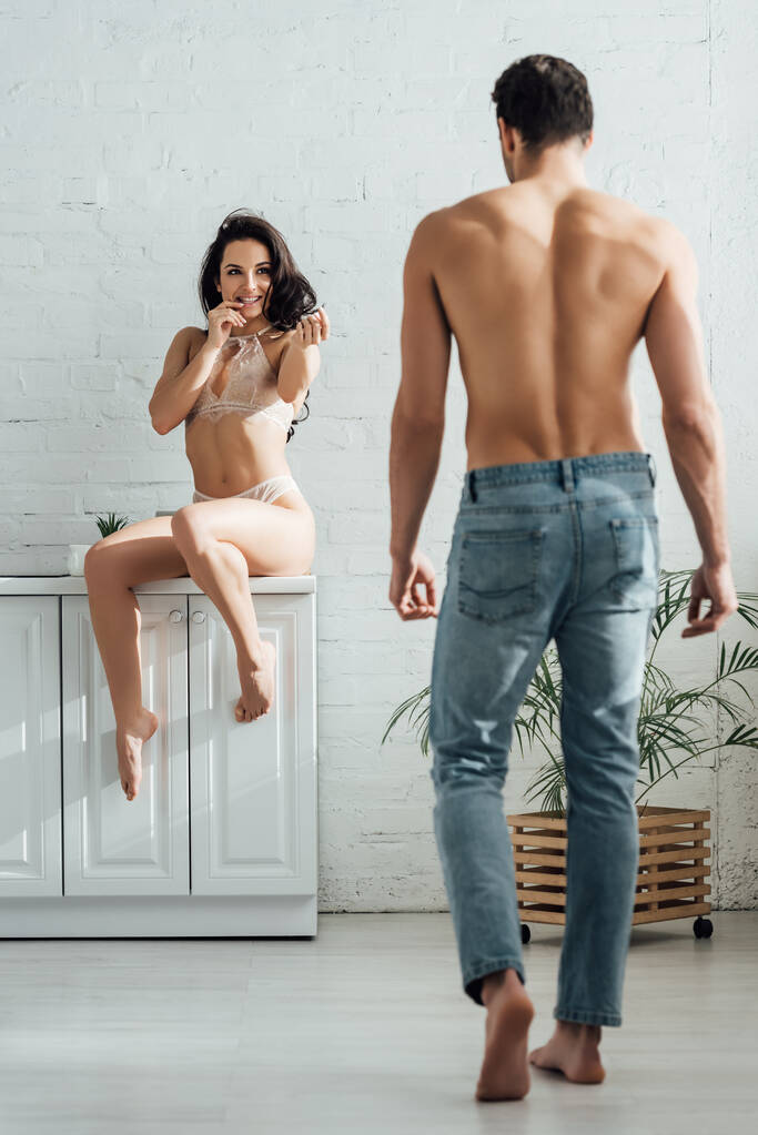 Сексуальная женщина улыбается, сидит на кухонном шкафу и смотрит на парня
 - Фото, изображение