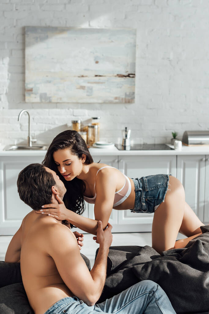 Sexy woman kissing boyfriend on sofa in kitchen - Photo, Image