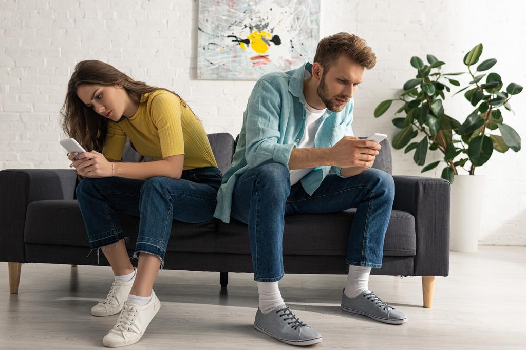 Зависимая пара с помощью смартфонов на диване в гостиной
 - Фото, изображение