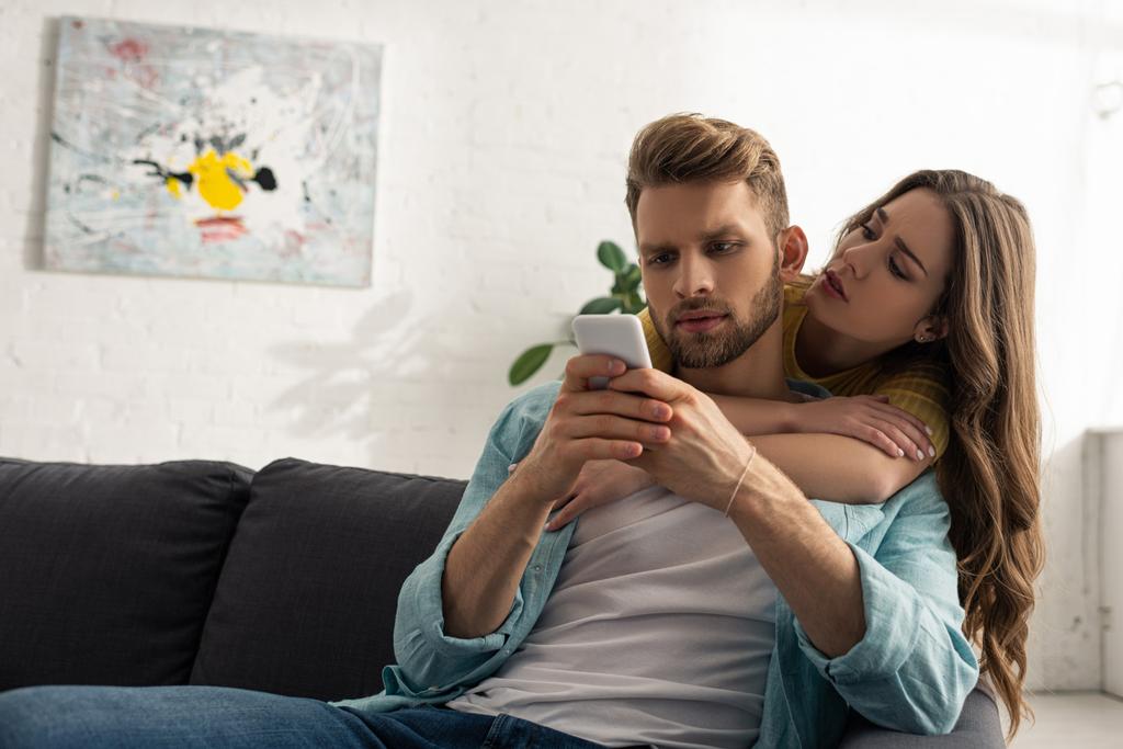 Belle femme embrassant petit ami accro avec smartphone sur le canapé
  - Photo, image