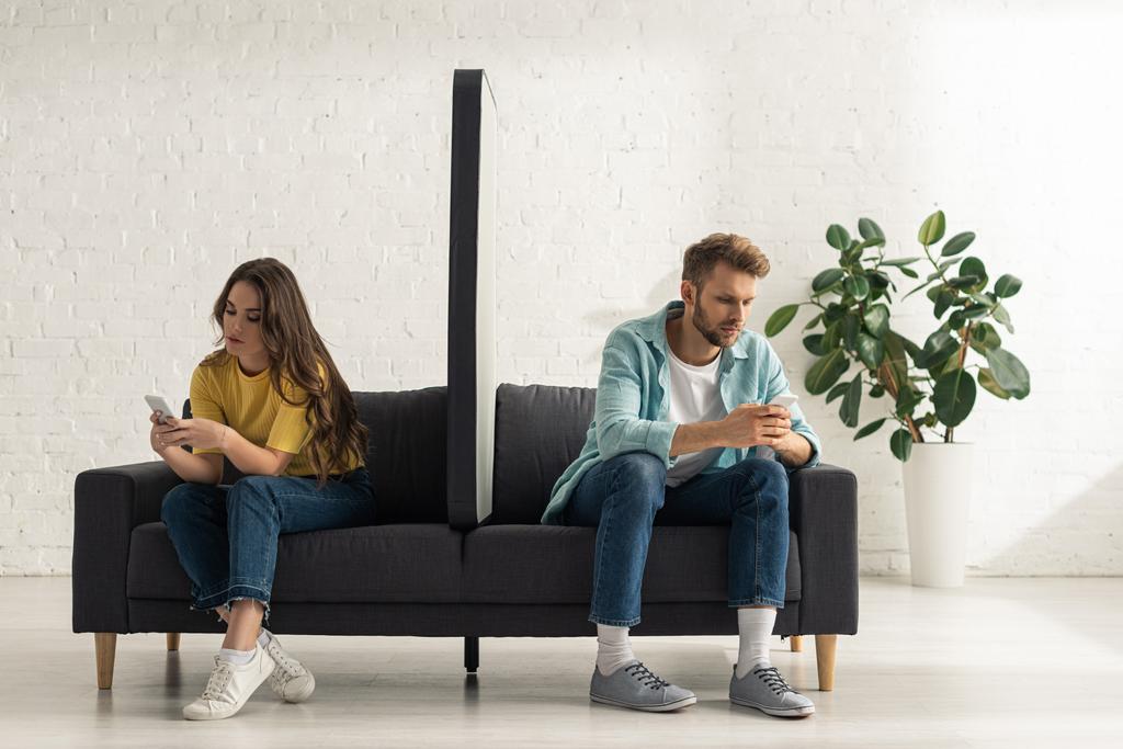 Model of smartphone on couch between young couple using smartphones in living room - Photo, Image