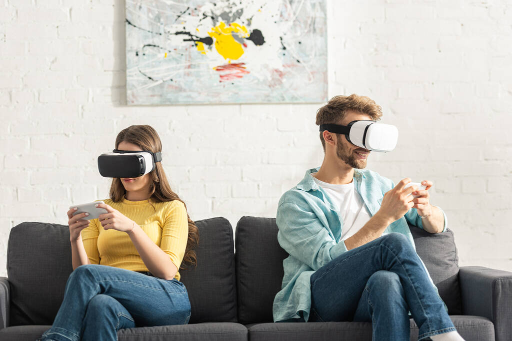 VR kulaklıklı genç çift koltukta akıllı telefon kullanıyor.  - Fotoğraf, Görsel