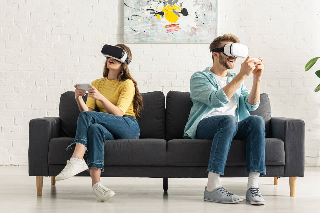 Casal usando fones de ouvido realidade virtual e smartphones no sofá
   - Foto, Imagem