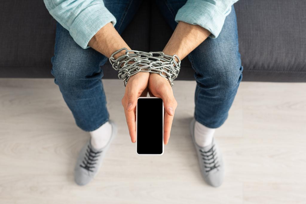 Vista superior del hombre con cadena alrededor de las manos sosteniendo el teléfono inteligente con pantalla en blanco
 - Foto, imagen