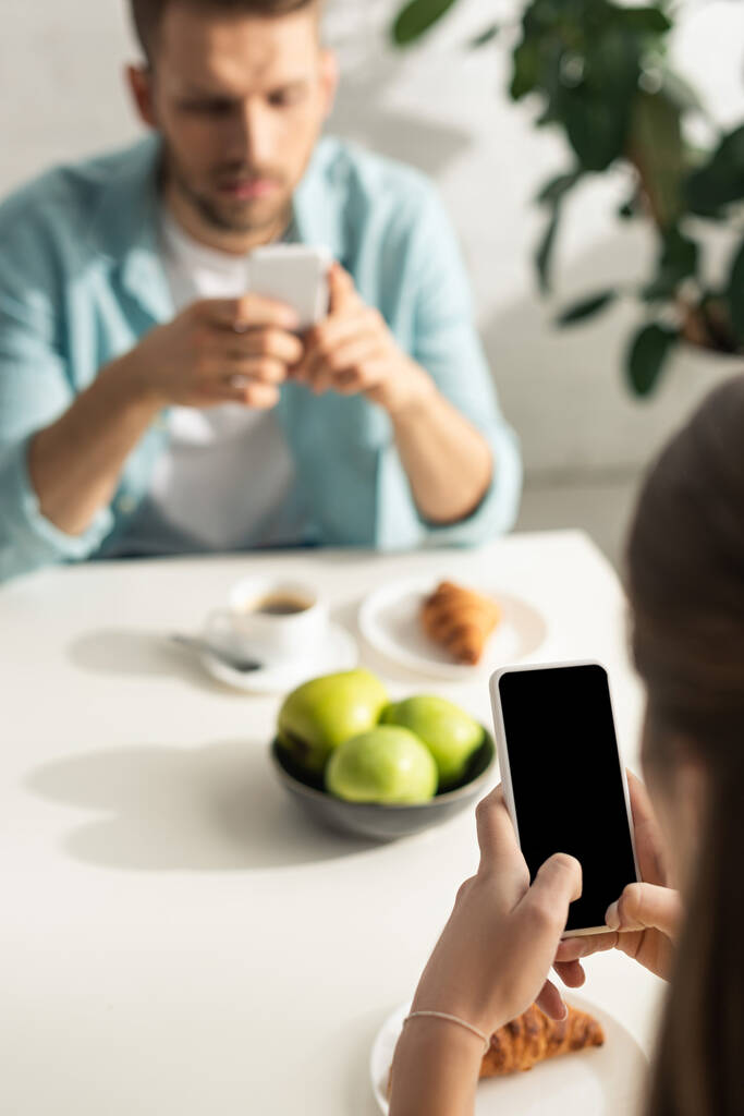Enfoque selectivo de la mujer usando smartphone con pantalla en blanco durante el desayuno con el novio
  - Foto, Imagen
