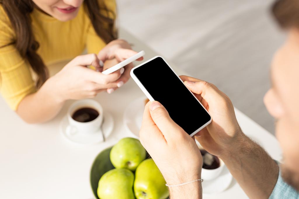 Enfoque selectivo de la pareja joven usando teléfonos inteligentes durante el desayuno
  - Foto, imagen