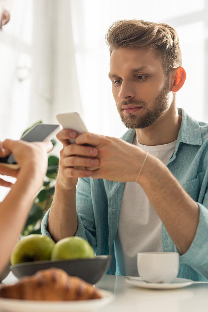 Enfoque selectivo de pareja adicta sosteniendo teléfonos inteligentes cerca de café y croissant en la mesa
  - Foto, imagen