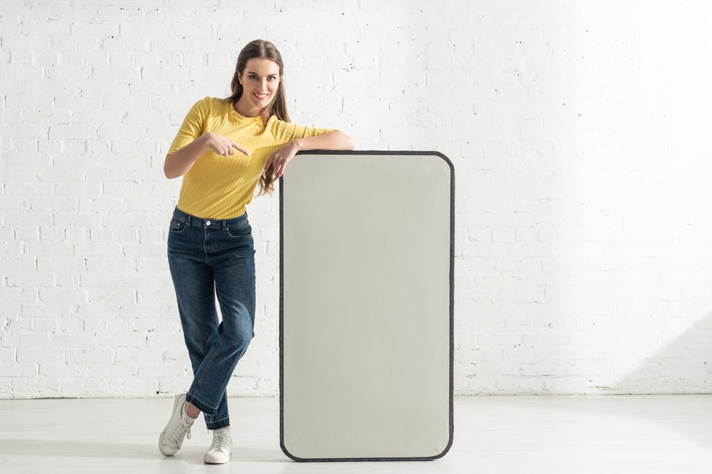 Smiling woman pointing with finger at model of smartphone  - Photo, Image