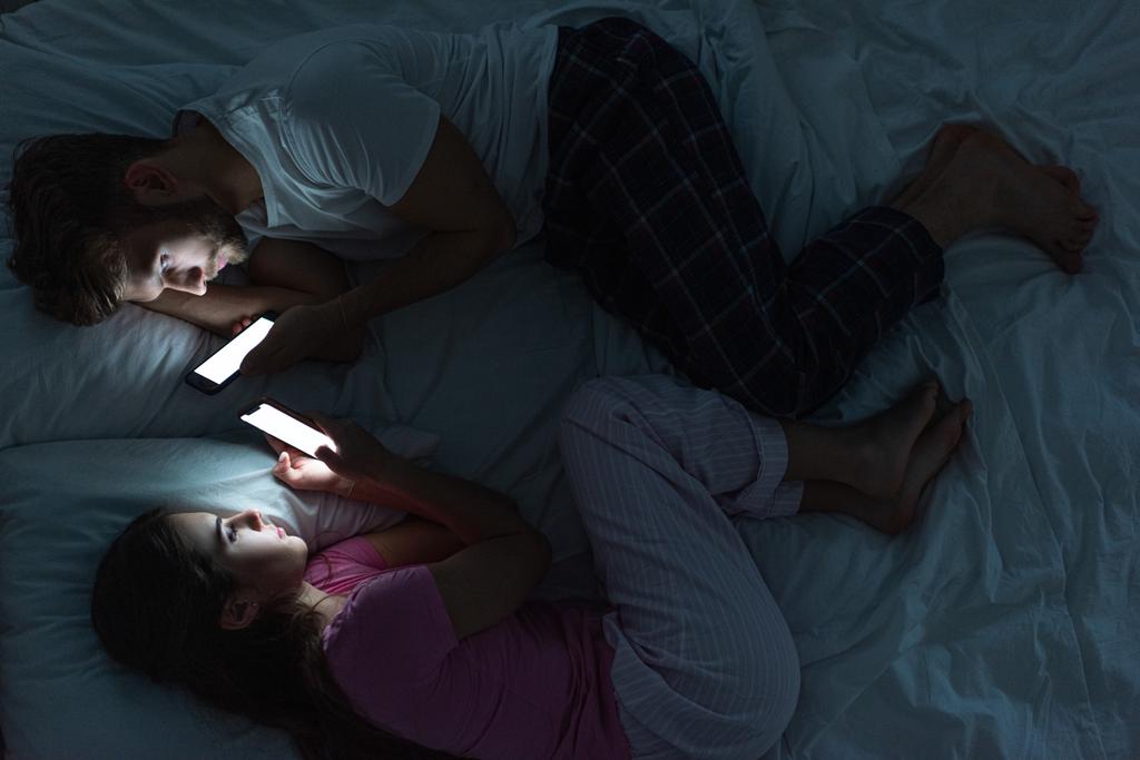 Вид зверху пари лежить на ліжку зі смартфонами вночі
  - Фото, зображення