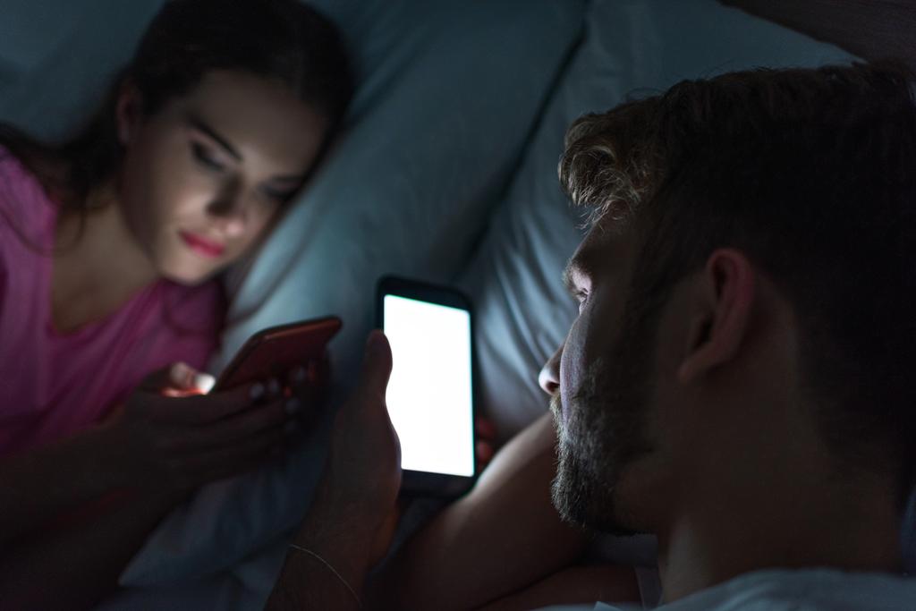 Selektywne skupienie mężczyzny korzystającego ze smartfona w pobliżu dziewczyny na czacie w nocy  - Zdjęcie, obraz