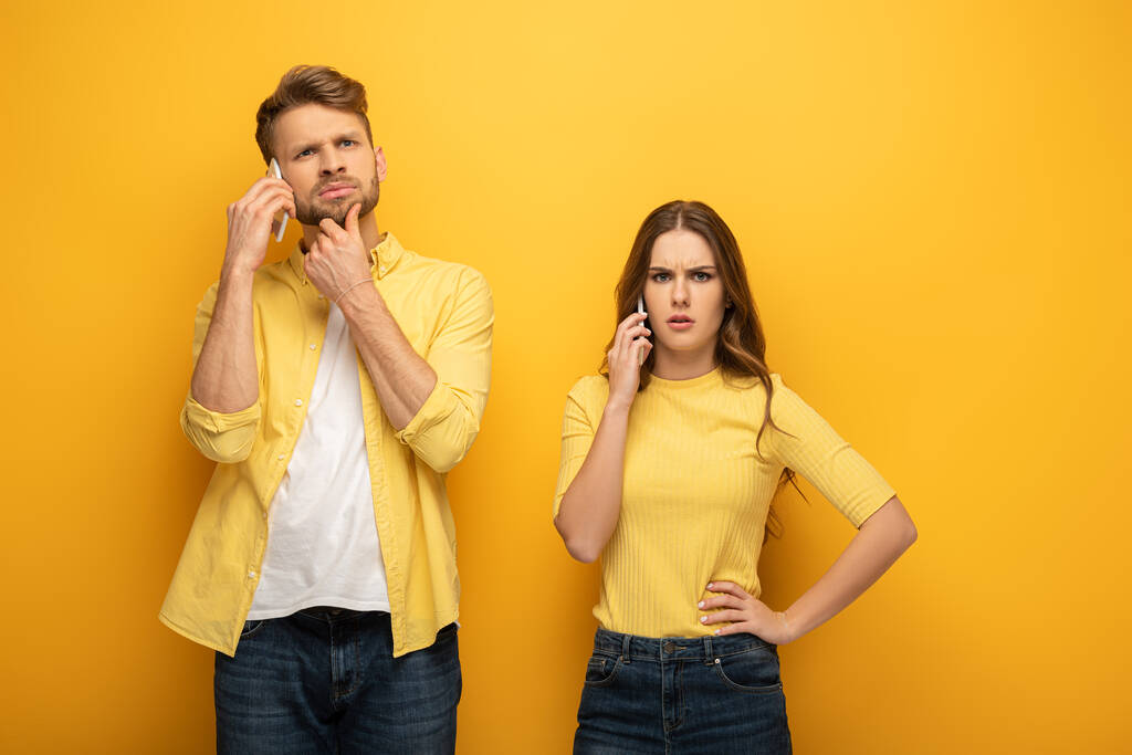 Confused couple talking on smartphones on yellow background - Photo, Image