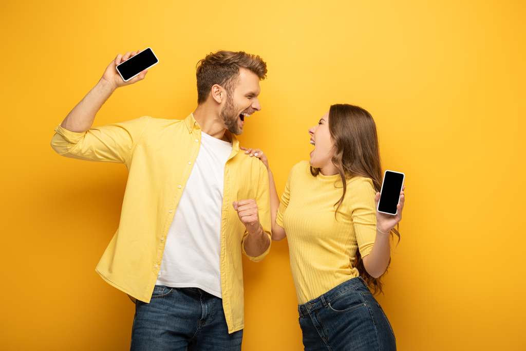 Jeune couple excité tenant des smartphones avec des écrans vides sur fond jaune
 - Photo, image