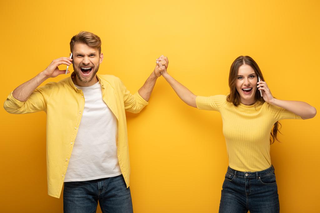 Šťastný pár high five při rozhovoru na chytrých telefonech na žlutém pozadí - Fotografie, Obrázek