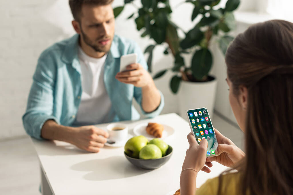 KYIV, UCRANIA - 21 de febrero de 2020: enfoque selectivo de la mujer que sostiene el teléfono inteligente con pantalla de iphone cerca de su novio charlando durante el desayuno
  - Foto, Imagen