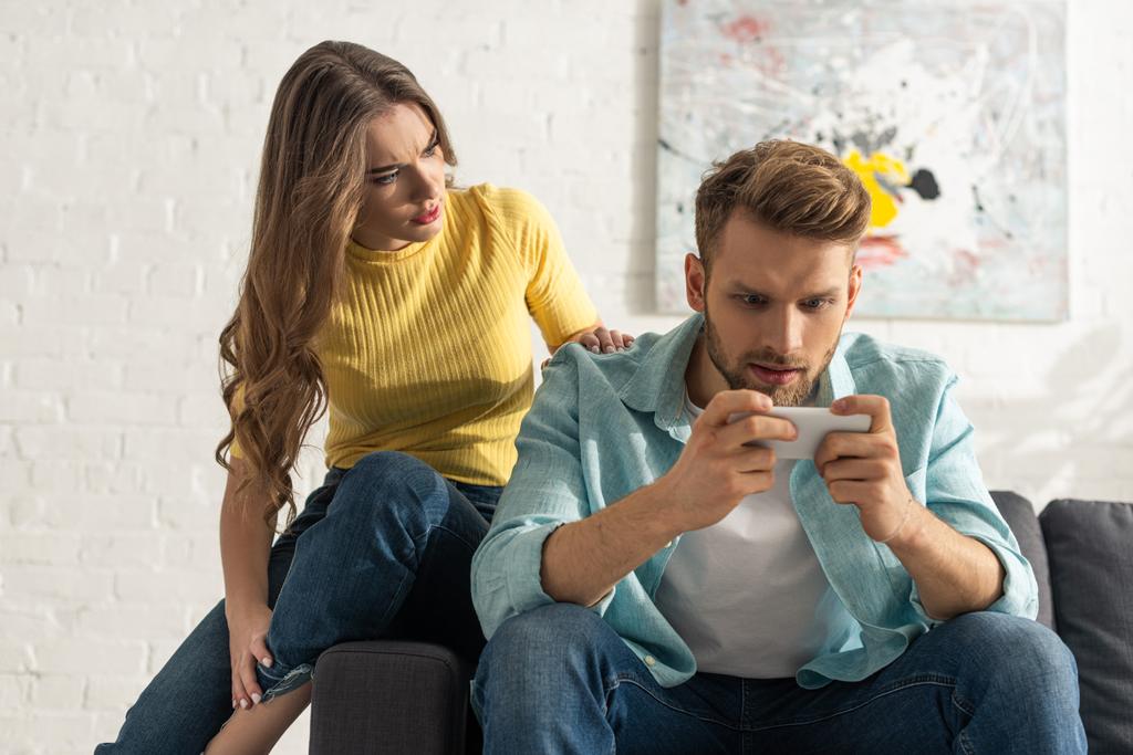 Worried girl sitting on couch near smartphone depended boyfriend  - Photo, Image